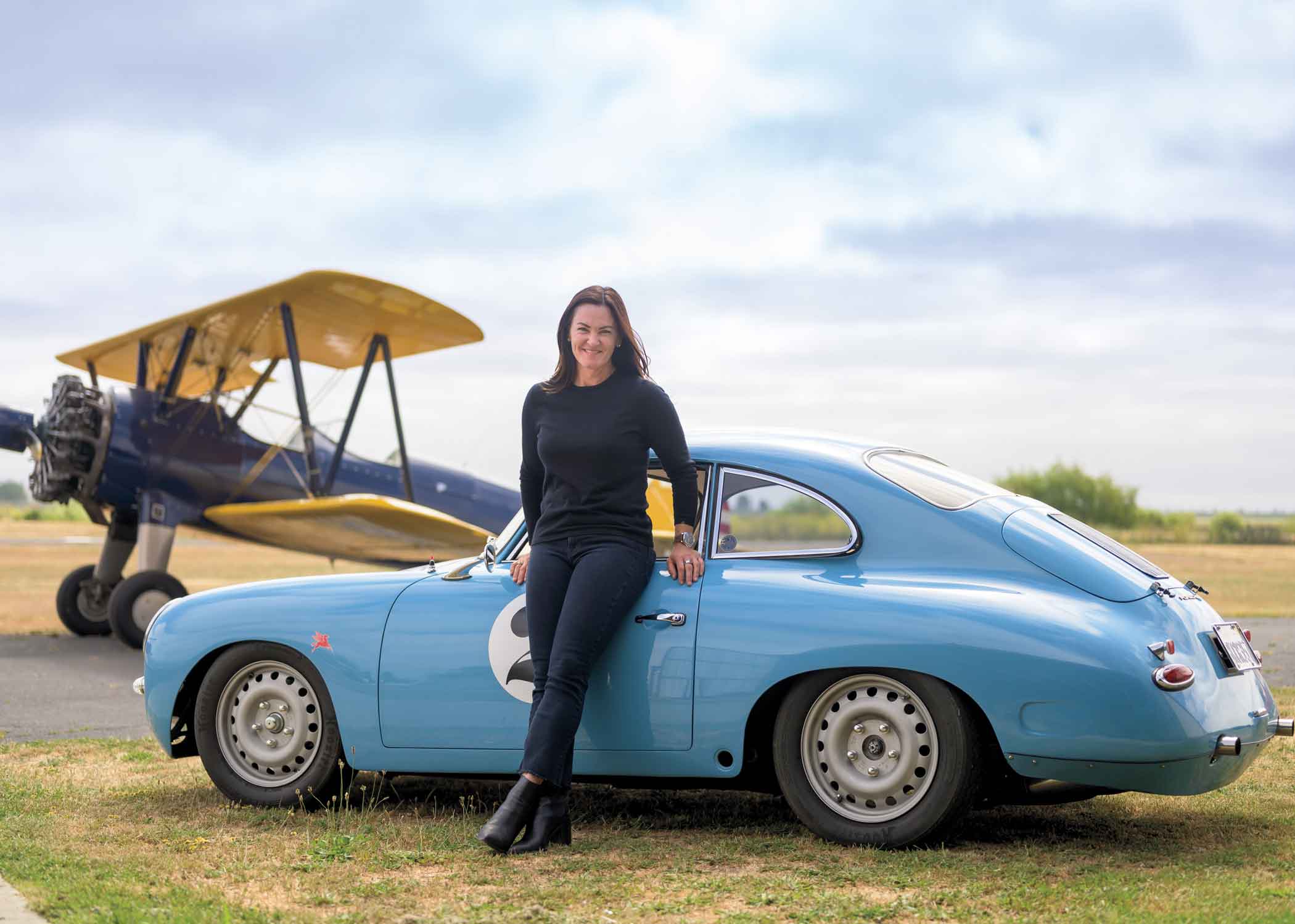 Shannon O'Shaugnessy leaning on a porsche with a plane in the background