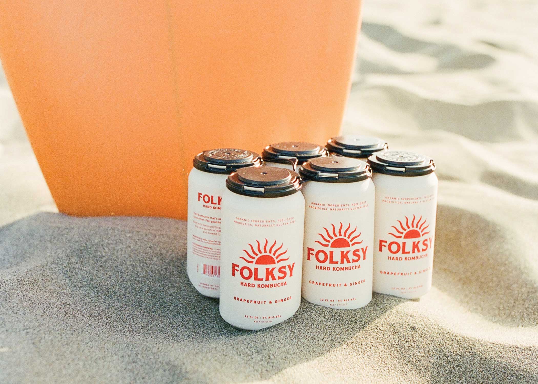 Folksy brand kombucha cans sitting on the sand